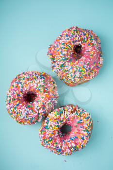 Three donuts with pink icing and candies on a blue pastel background