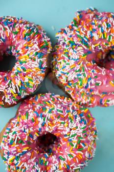 Three donuts with pink icing and candies on a blue pastel background