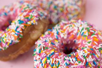 Close up of a three donuts with pink icing and candies on a pink pastel background