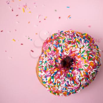 Close up of a donut with pink icing and candies on a pink pastel background