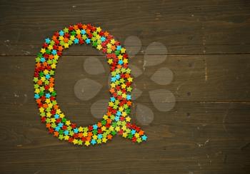 Letter Q from alphabet made with star shape candy on a wooden background