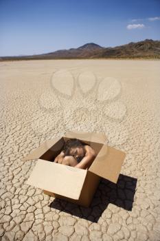 Royalty Free Photo of a Pretty Nude Young Woman Sitting in a Box in a Cracked Desert Landscape in California