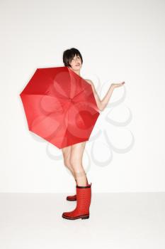 Royalty Free Photo of a Woman in Red Boots Holding a Red Umbrella and Checking for Raindrops