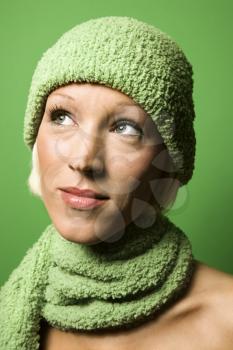 Head and shoulder portrait of smiling young adult Caucasian woman on green background wearing winter hat and scarf.