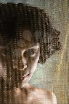 Nude Hispanic woman looking at viewer from behind sheer fabric.