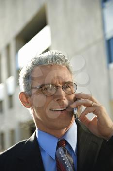 Prime adult Caucasian man in suit smiling and talking on cellphone in urban setting.