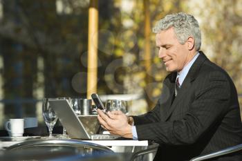 Royalty Free Photo of a Businessman Sitting Outside With a Laptop and Cellphone