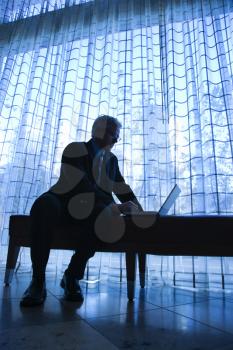 Royalty Free Photo of a Businessman in a Suit Sitting on a Bench Typing on a Laptop