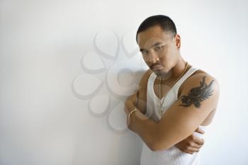 Royalty Free Photo of a Portrait of an Asian Man Leaning Against a White Wall With arms Crossed