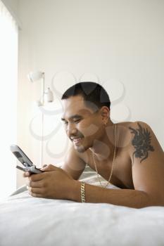 Royalty Free Photo of a Man Lying on a Bed Messaging on a Cellphone