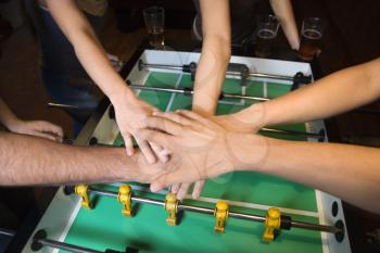 Royalty Free Photo of a Group of Friends Clasping Hands Over a Foosball Table