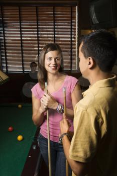 Young man and woman talking and smiling while playing billiards.