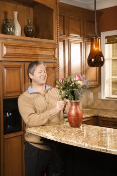 Royalty Free Photo of a Man Smiling and Arranging Flowers in a Vase in a Kitchen