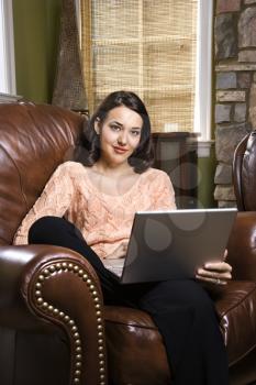 Caucasian/Hispanic young woman sitting in leather chair with laptop looking at viewer.