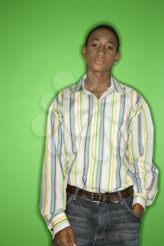 Portrait of African-American teen boy with one hand in pocket standing against green background.