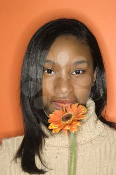 Portrait of African-American teen girl holding single Gerbera Daisy against orange background.