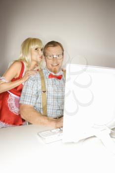 Royalty Free Photo of a Blonde Woman Dressed in a French Maid Outfit Whispering to a Man Sitting at a Computer Dressed Like a Nerd