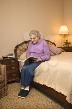 Royalty Free Photo of an Elderly Woman in a Bedroom at a Retirement Community Center Reading a Book