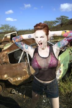 Royalty Free Photo of a Tattooed Woman Yelling and Covering Her Ears in a Junkyard