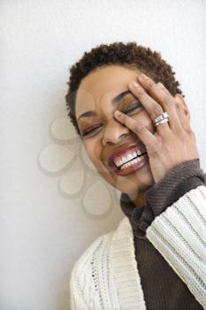 Royalty Free Photo of a Woman Standing Against a White Wall Smiling With Hand on Hace and Eyes Closed