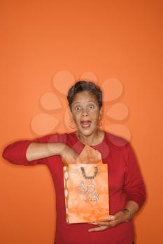 Royalty Free Photo of an Older Woman With Her Hand in a Gift Bag Looking Surprised
