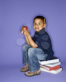 Royalty Free Photo of a Boy Sitting on a Stack of Books Holding an Apple