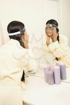 Royalty Free Photo of a Woman Looking in the Mirror Adjusting an Eye Mask