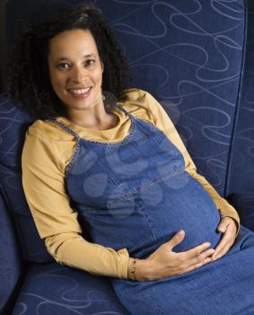 Portrait of young pregnant female with hands on stomach and looking at viewer.