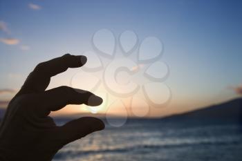 Royalty Free Photo of a Hand in the Foreground With Fingers Around the Sunrise Over the Coast of Kihei, Maui, Hawaii, USA
