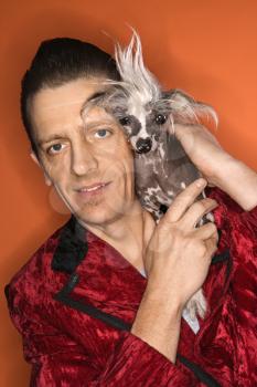 Royalty Free Photo of a Man Wearing a Velvet Jacket and Holding a Chinese Crested Dog