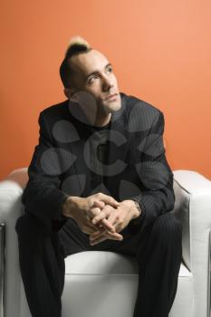 Royalty Free Photo of a Man in a Suit With a Mohawk Sitting in a Chair Against an Orange Background