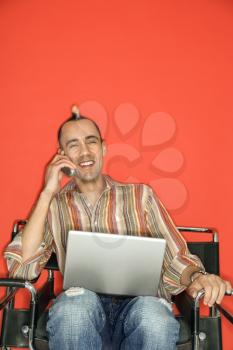 Royalty Free Photo of a Man With a Mohawk Holding a Laptop Talking on a Cellphone