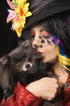 Royalty Free Photo of a Woman in Unique Makeup Holding and Kissing a Black Pomeranian Dog