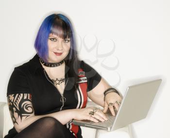 Royalty Free Photo of a Tattooed Woman With Blue Hair Typing on a Laptop