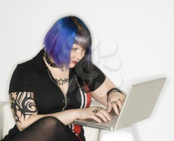Royalty Free Photo of a Tattooed Woman With Blue Hair Typing on a Laptop