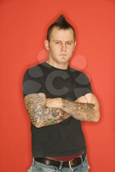 Royalty Free Photo of a Man With a Mohawk and Tattoos Standing With Arms Crossed