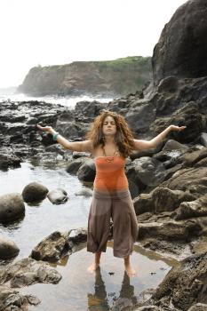 Royalty Free Photo of a Woman Standing on a Rocky Shore With Arms Outstretched and Eyes Closed