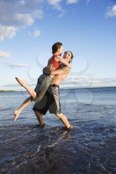 Caucasian young adult couple frolicking on beach.