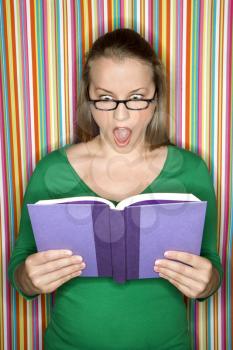 Young Caucasian female adult reading book making expression.
