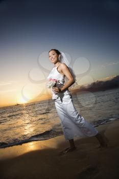 Royalty Free Photo of a Bride at Sunset Holding a Bouquet on a Beach
