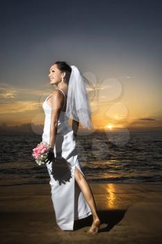 Royalty Free Photo of a Young Bride at Sunset Holding a Bouquet on a Beach
