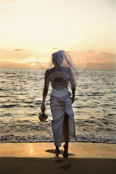 Young adult female Caucasian bride standing on beach at sunset.