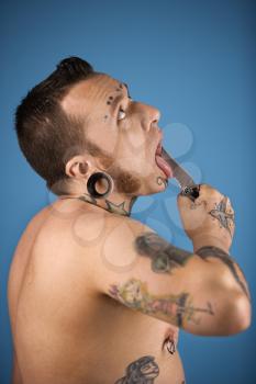 Royalty Free Photo of a Tattooed Man Holding a Knife to His Tongue