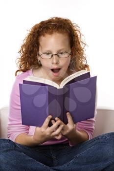 Royalty Free Photo of a Little Girl Sitting and Reading Book Looking Surprised