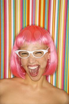 Portrait of attractive Caucasian young adult woman wearing pink wig against striped background making sassy expression looking at viewer.