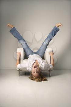 Royalty Free Photo of a Woman in Blue Jeans Lying Upside Down on a Chair With Legs in the Air Laughing