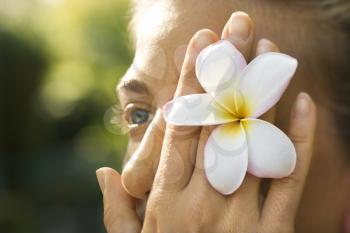Royalty Free Photo of a Woman Holding a Plumeria Flower Over Her Eye