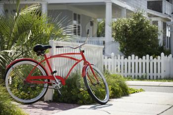 Royalty Free Photo of a Red Beach Cruiser Bicycle Propped Against a Fence in Front of a House