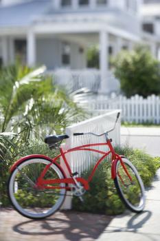 Royalty Free Photo of a Red Bike Leaning Against a Fence in Front of a House