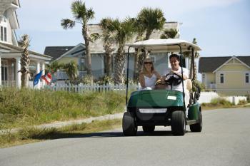 Royalty Free Photo of a Man and Woman Driving a Golf Cart Down a Residential Street